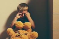 Scared boy crying in corner with toy bear Scared boy crying in corner with toy bear