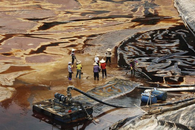Photo : Sur une masse de sable, terre, et d'une masse noire, des ouvriers nettoient les dégâts d'une mine de cuivre à Shanghang, dans la province de Fujian, en juillet 2010.